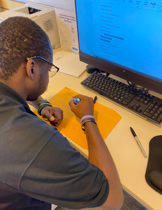 Ugo writes on a manila envelope while sitting at a desk. 