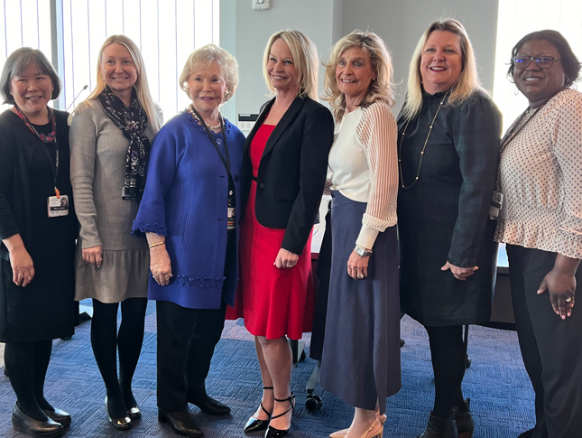 Seven women stand for a photo and smile. 