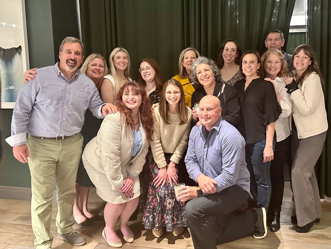 A large group of people stand in front a green curtain and smile at the Council of Parent Attorneys and Advocates (COPAA) conference.