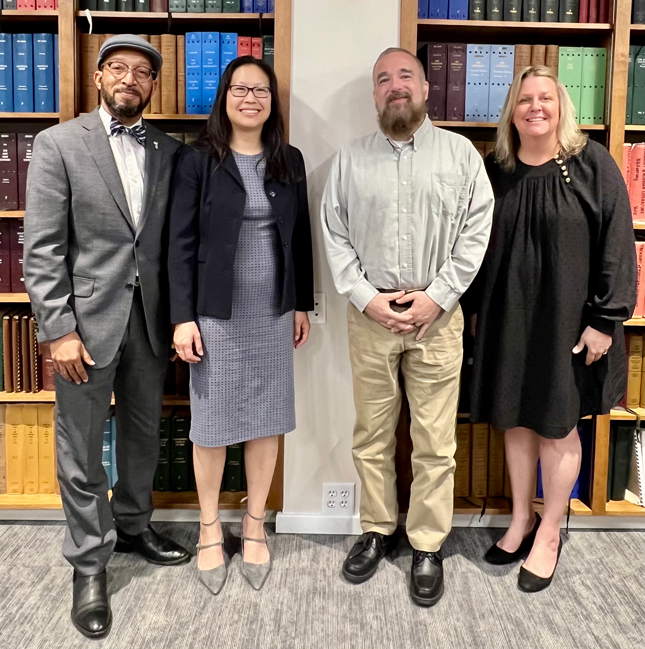 Maureen van Stone and three other individuals smile in a group photo at the U.S. Department of Education at the Disability Rights Bar Association conference. They are standing in front of bookcases filled with books.