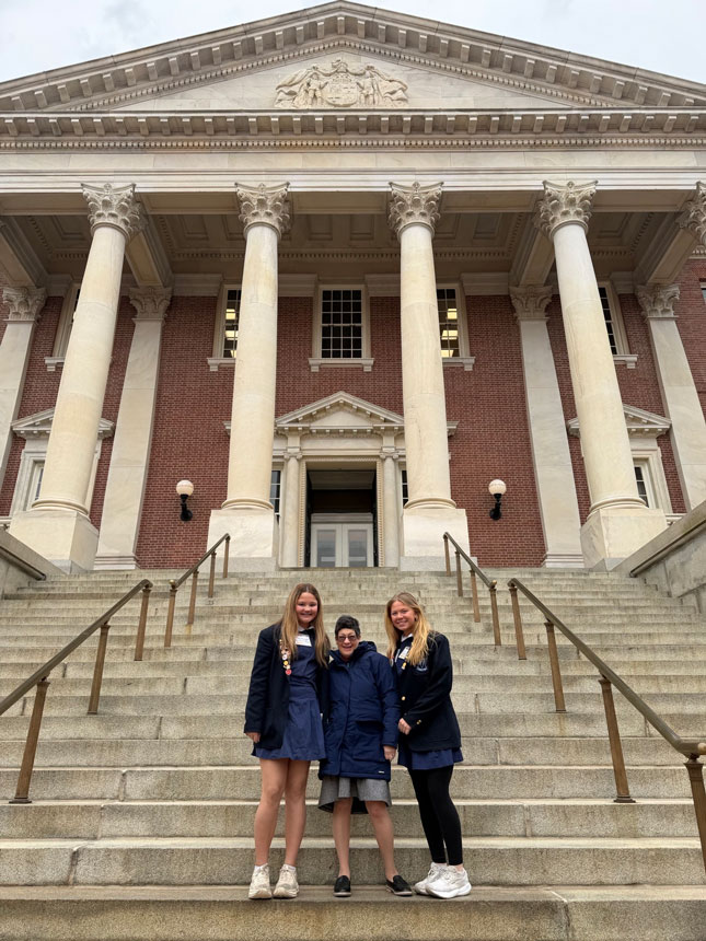 Three women stand on the steps of the Maryland State House.