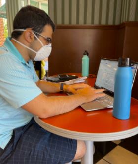 A young man works at a laptop while wearing a face mask.