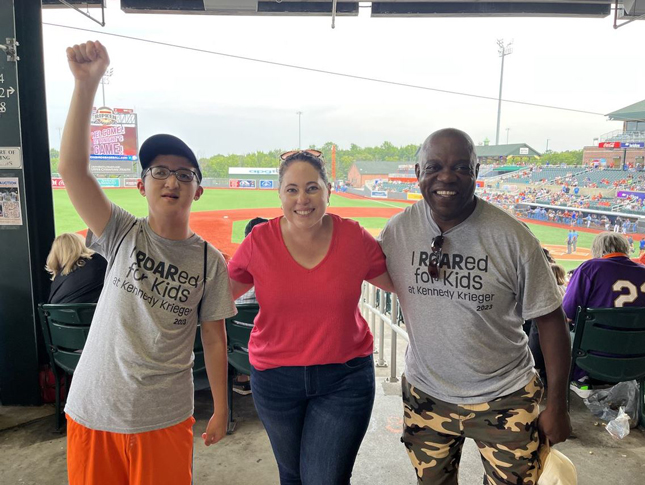 Three Night at the Ballpark attendees stand for a photo on the concourse at Leidos Field at Ripken Stadium. The playing field can be seen behind them.