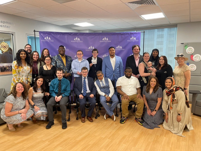 A group of 2023 Project SEARCH Graduation ceremony attendees standout in front of a purple backdrop with the Kennedy Krieger Institute logo.