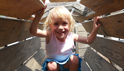 A young girl smiles while playing on playground equipment.