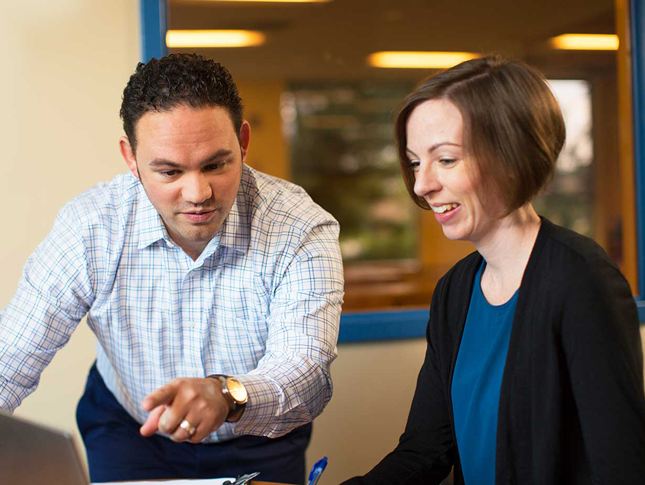 Two teachers review information on a laptop monitor.