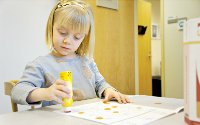 A little girl completes an activity using a highlighter and a piece of paper.