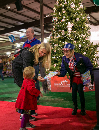 A festival of trees volunteer hands a paper to a mother and her young daugther.
