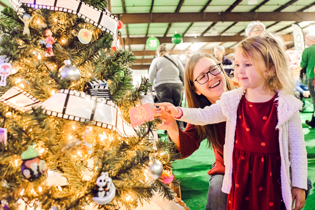 A mother and daughter smile while looking at Christmas trees.