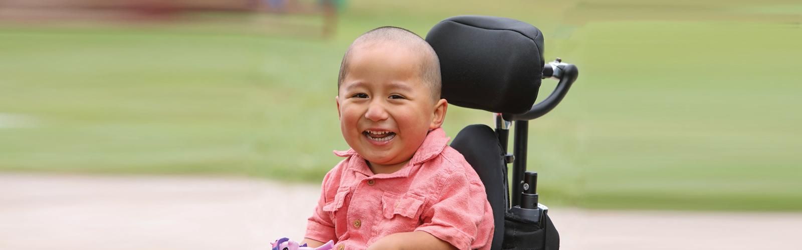 A young boy sitting in a wheelchair smiles.