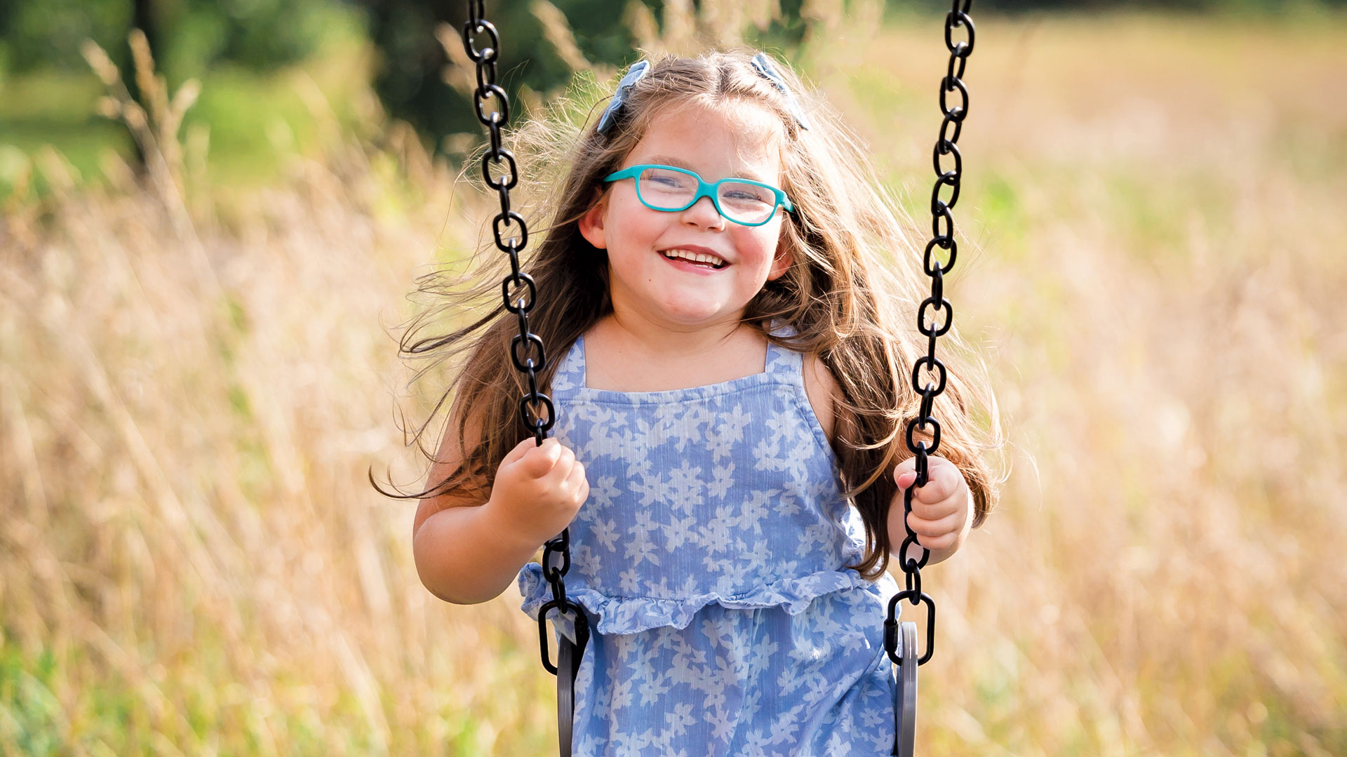 A young girl smile while sitting on a swing.
