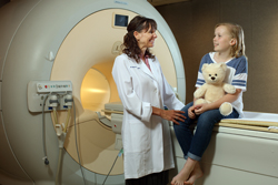 A doctor with a child sitting on an MRI machine.