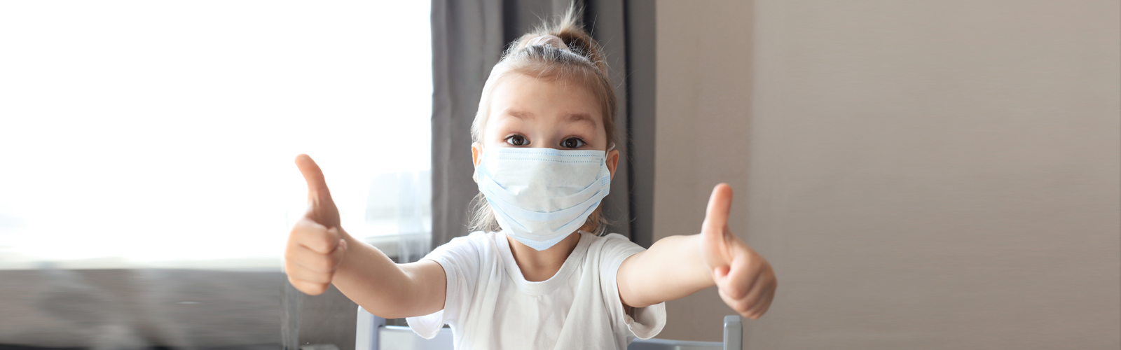 Little girl in a mask with thumbs up.