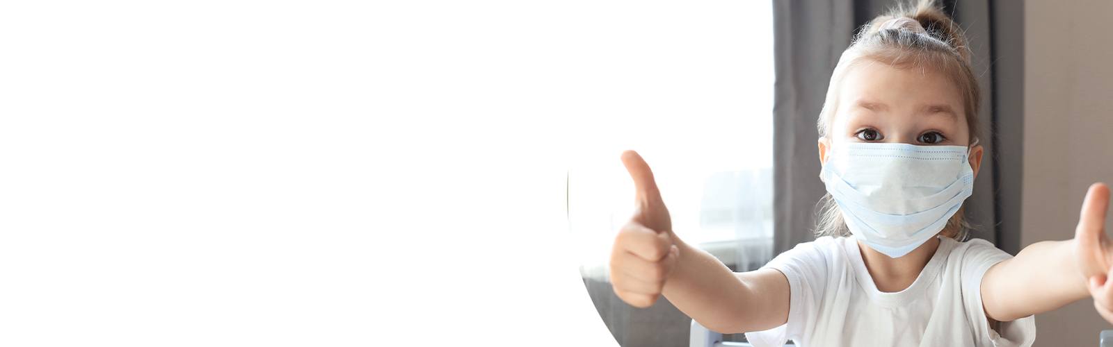 Little girl in a mask with thumbs up.