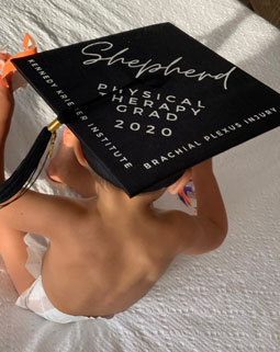 Toddler wearing graduation cap sits with back to camera.