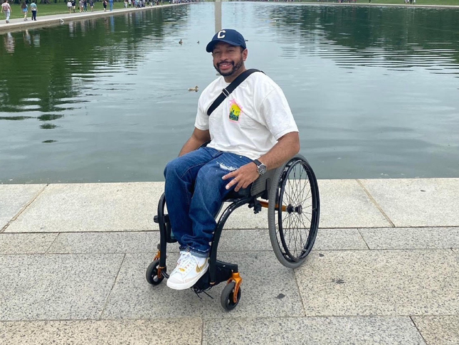 An adult with spina bifida smiles while sitting in his wheelchair.
