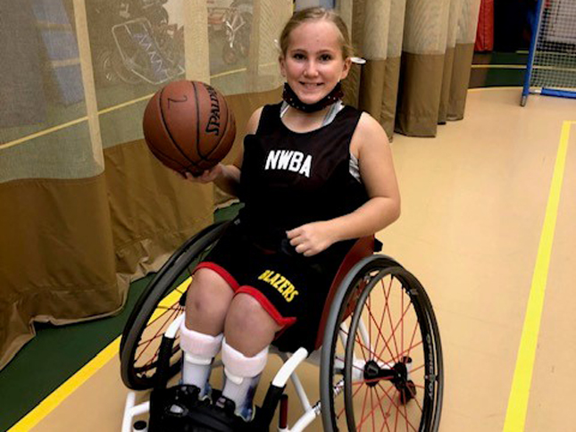 An adaptive sports athlete sits in her wheelchair while holding a basketball.
