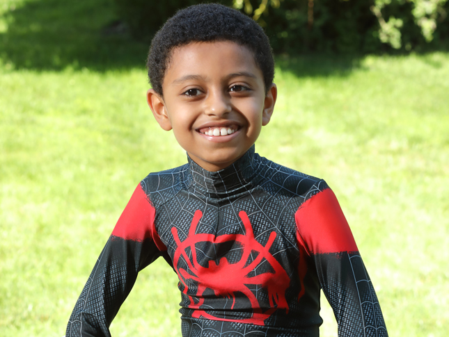 A young boy sits on a bench outside and smiles.