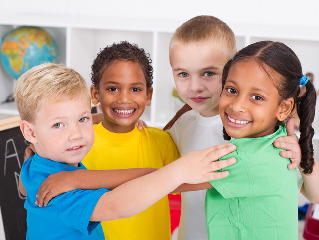 Four smiling pre-k students stand in a circle with their hands on each other's shoulders.