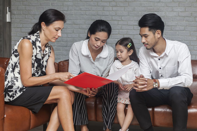 A mental health professional reviews the contents of a folder with a mother, father and their young daughter.