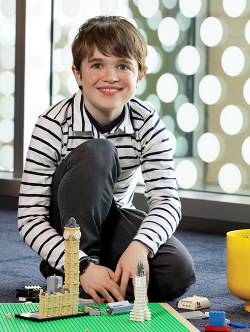 Dylan, a patient, smiles in front of his Lego buildings.