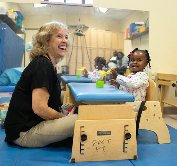 A patient sits at a table, with her therapist next to her, during a therapy session.