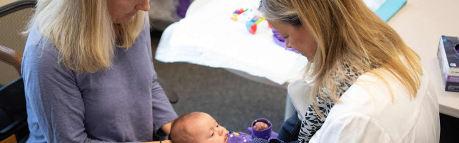 Two women treating an infant. 