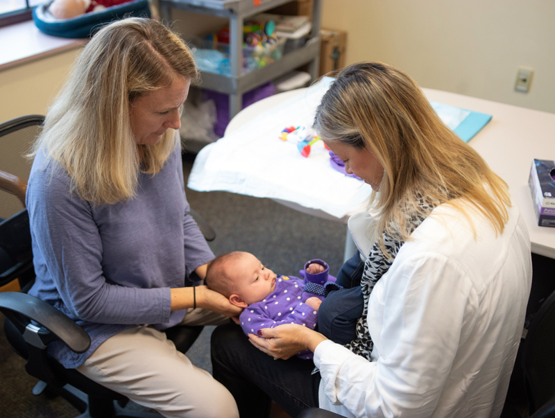 An infant is held by a therapist, with her head being held up by another, during a therapy session.