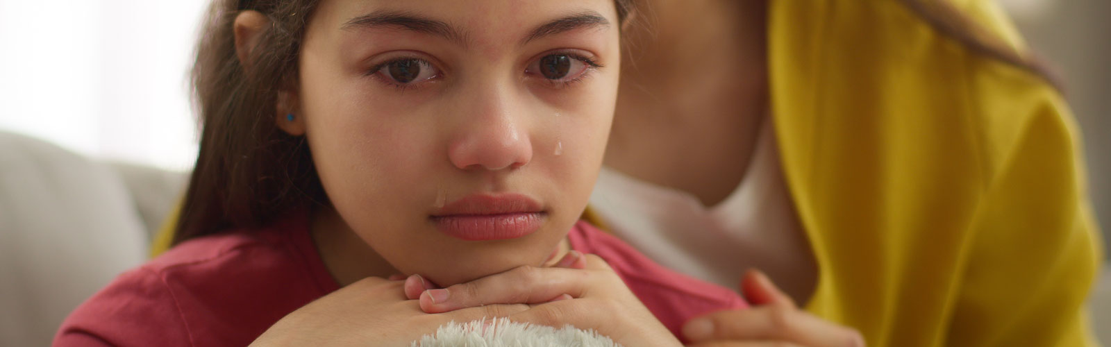 A sad little girl sheds a tear while being comforted by her mother.
