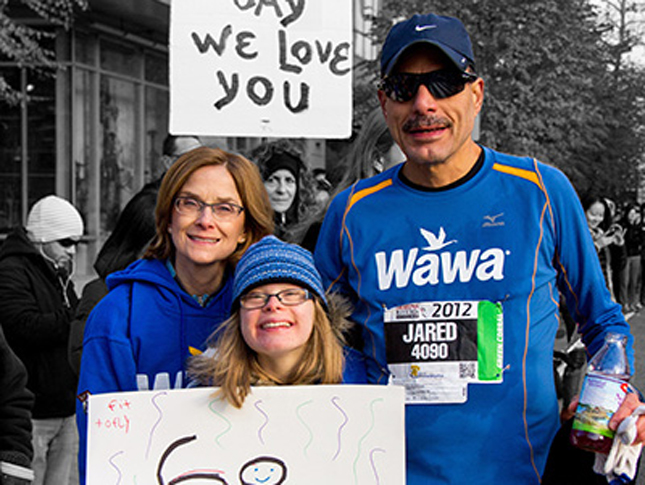 A father, mother and daughter pose for a photo at a marathon. The father is wearing a running suit.