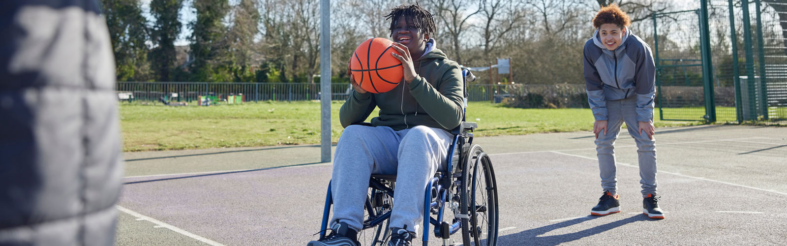 A teenaged boy in a wheelchair playing basketball.