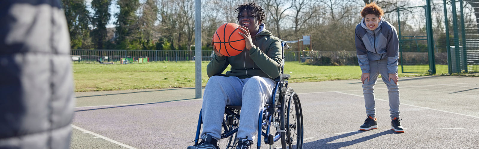 A teenaged boy in a wheelchair playing basketball.