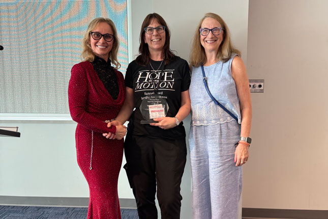 India Morrison stands between Dr. Cristina Sadowsky and Janet Dean. All three are smiling as Morrison holds the Janet Dean Improving Lives Award.