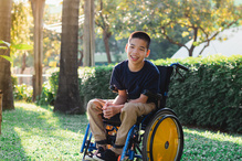 A young boy sits in a wheelchair smiling. 