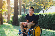A young boy sits in a wheelchair smiling.