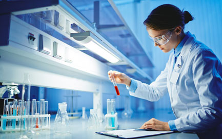 A young woman works with liquids in glassware in a research lab.