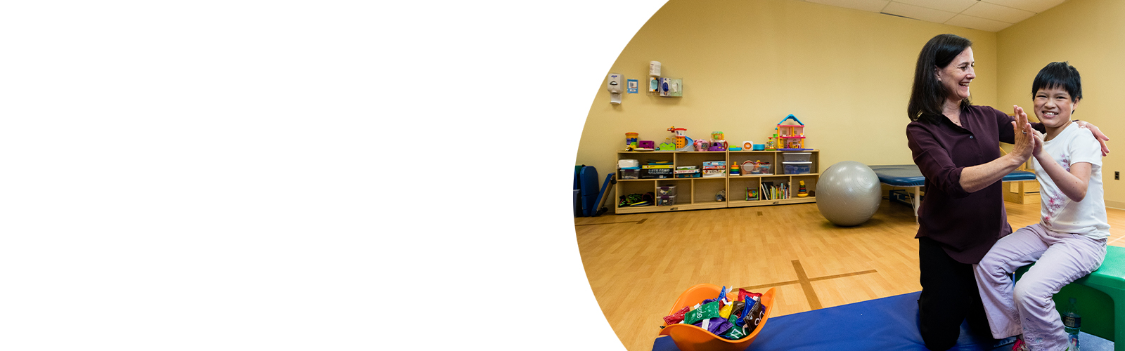 An occupational therapist and her patient, a little girl, smile and high five each other during a therapy session.