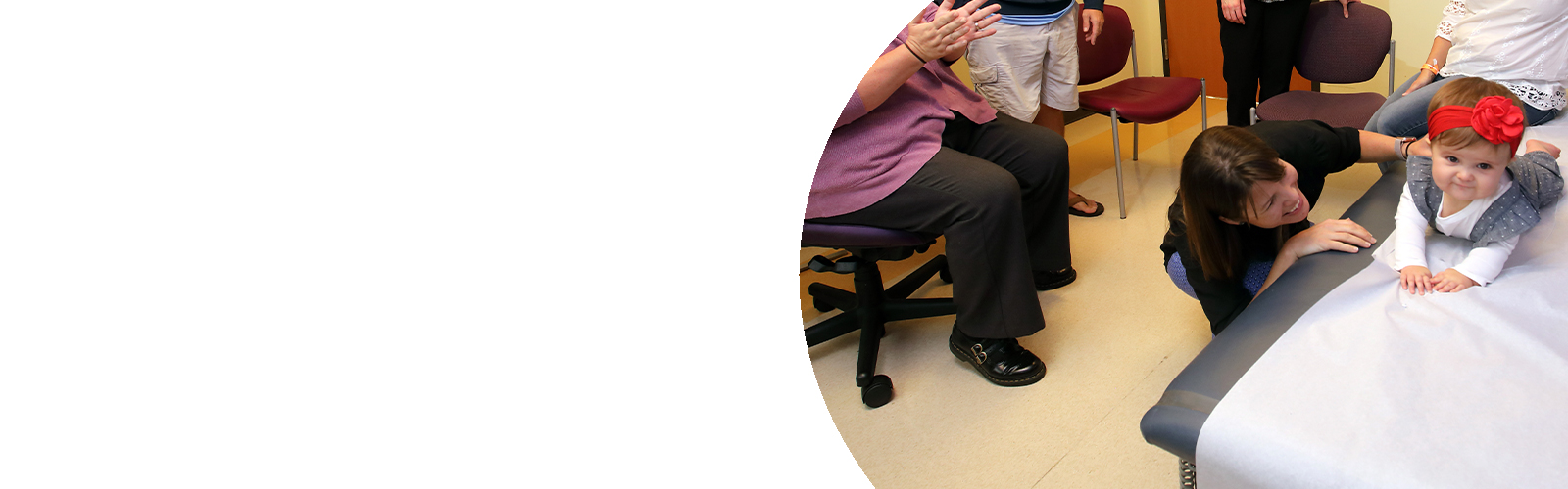 A baby lays on her stomach on an examination table, while her doctor supports her back.