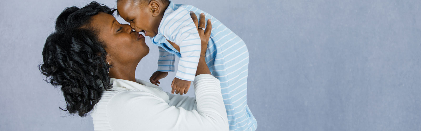 A woman kisses an infant as she holds him up.