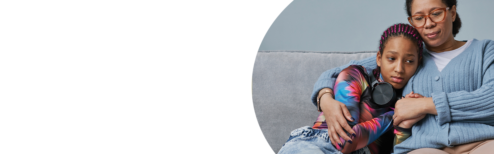 A girl is comforted by her mother while sitting on a sofa.