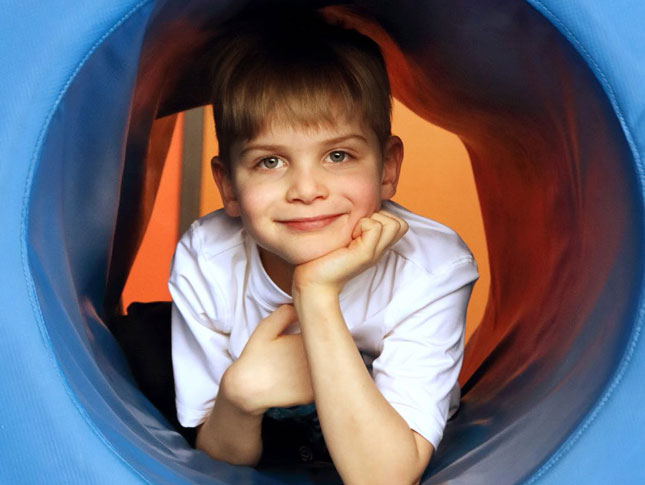 A boy poses for a photo inside of a play tunnel.