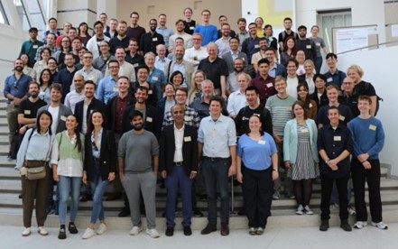 A group photo from the 10th international CEST Workshop. The photo is taken on a set of stairs inside of a lobby-like setting, with people standing on individual levels of the staircase.