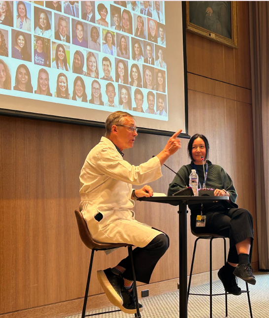 Dr. Justin McArthur and Dr. Catherine Chu sit at a table under a projection screen during their interview.
