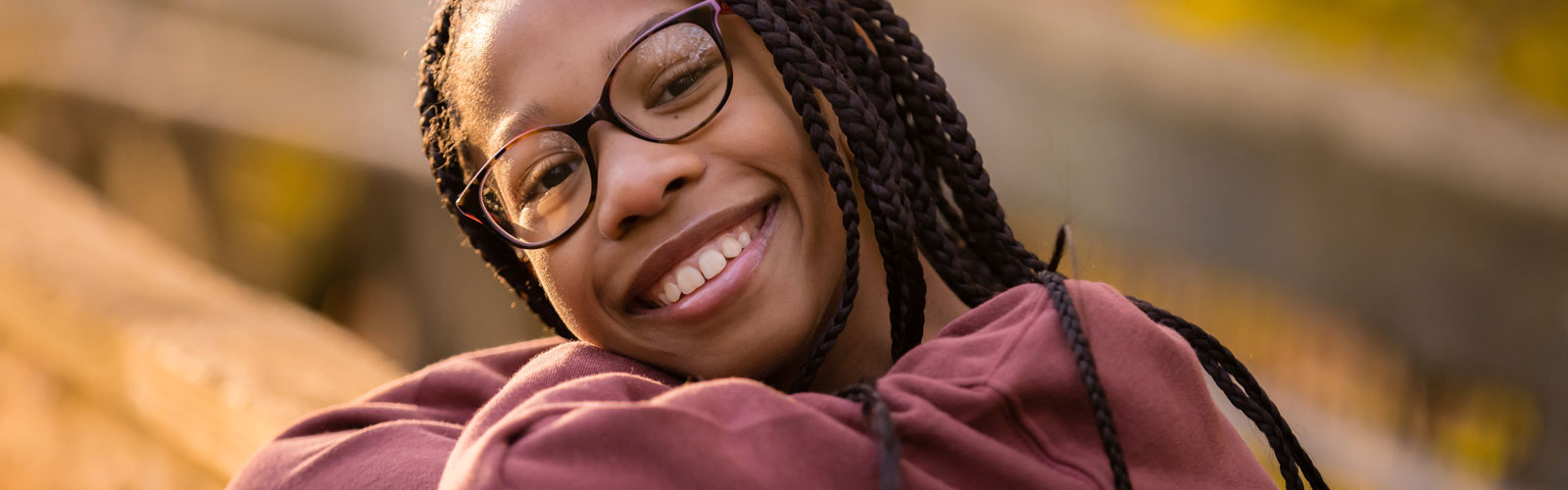 A child wearing glasses leans against a railing and smiles.
