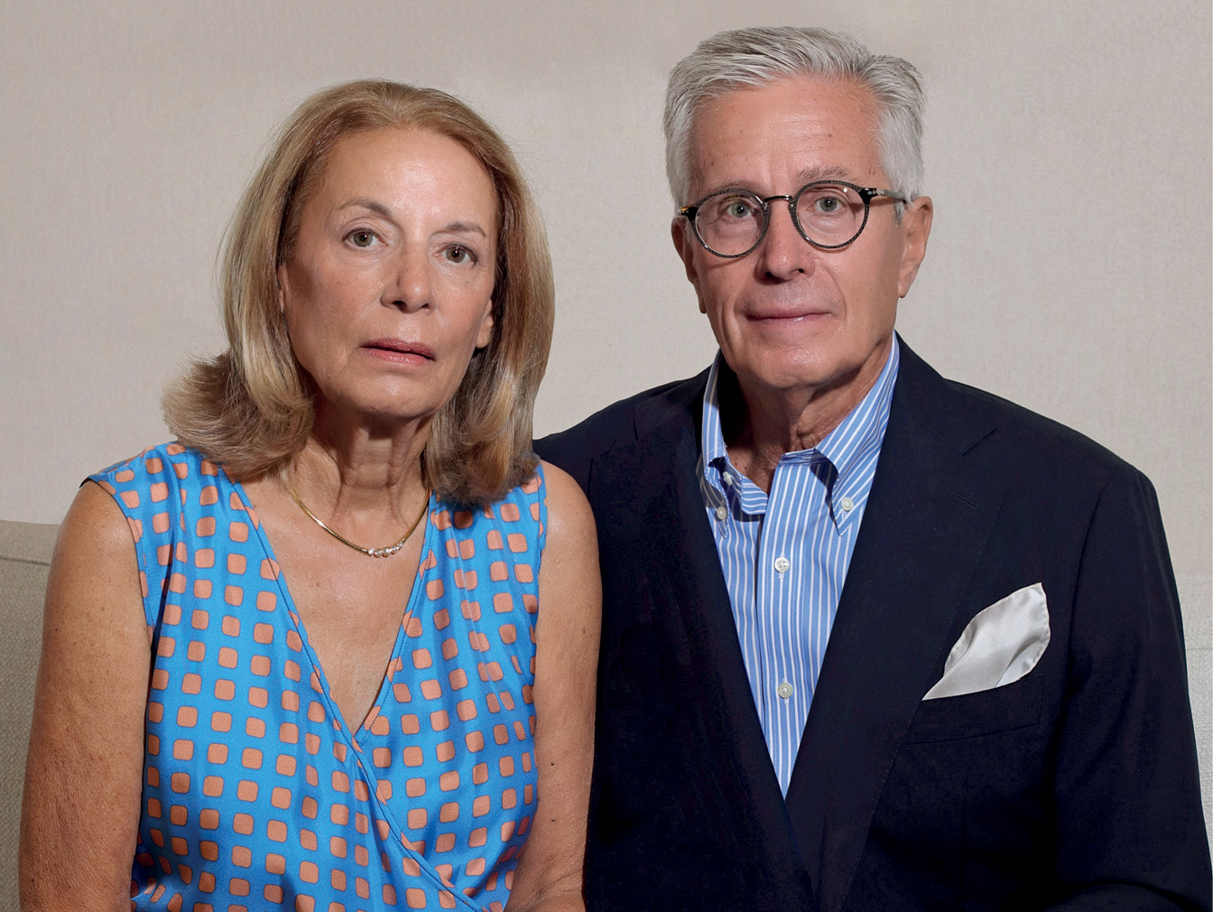 Portrait photo of a woman wearing a dress and necklace and a man wearing glasses and a suit with no tie