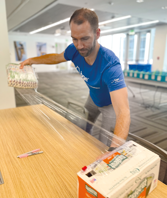 A man wraps diapers for care packages. He is wearing a blue T-shirt that says “BGE, an Exelon Company.”