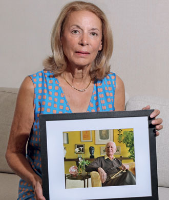 A woman sitting in a chair holds a framed photo of her father.