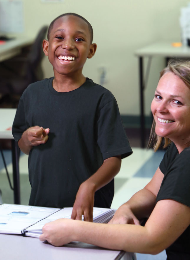 A student and his female teacher work on a matching activity at a desk in a classroom at Kennedy Krieger High School.