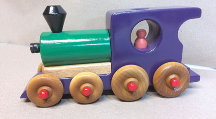 A wooden toy train locomotive in purple, green, pink, red and black, along with natural, unpainted wood.