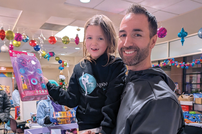 A little girl holds a toy from Kennedy Krieger while being held by her father.